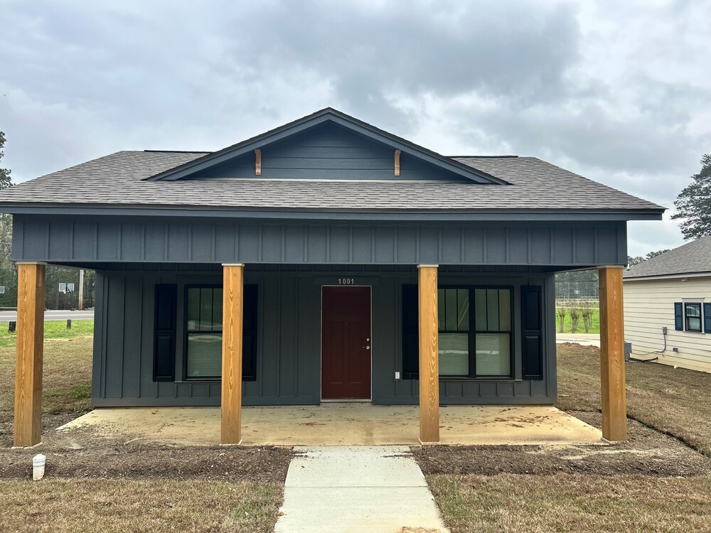 Front of a grey house with four wooden pillars on the front.