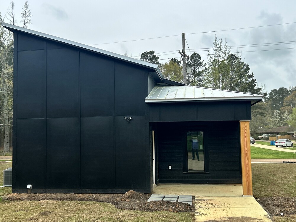The side of a black house with A door on the right side, and the roof being higher on the left side.