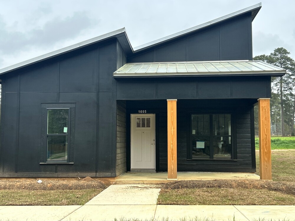 A front view of a black house with a door in the middle, two wooden pillars in the front, and the roof higher on the right.